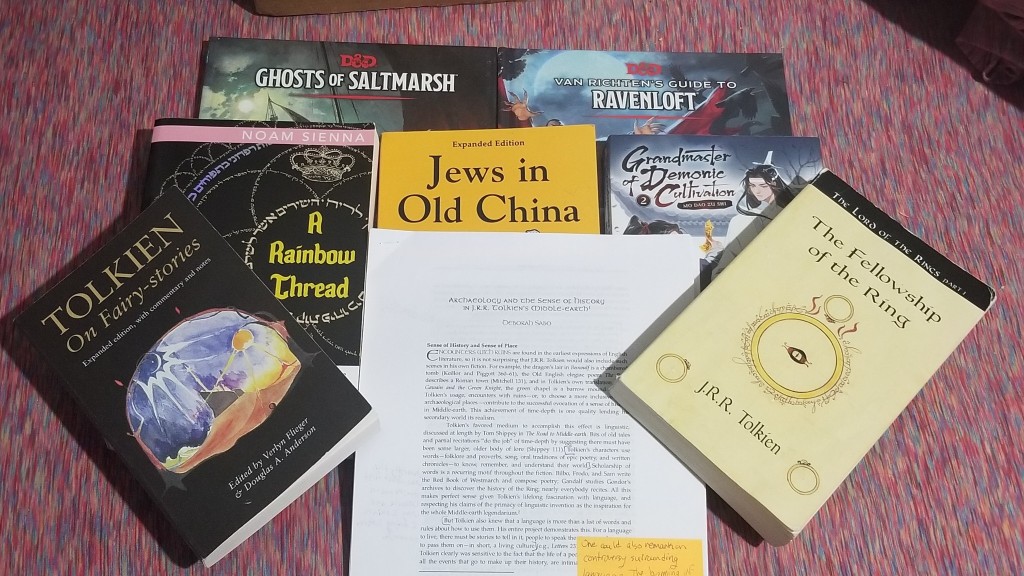 A pile of books and papers. The bottom later is the D&D books "Ghosts of Saltmarsh" and "Van Richten's Guide to Ravenloft," only the titles can be seen. The middle layer is, from left to right, "A Rainbow Thread," "Jews in Old China" and "Grandmaster of Demonic Cultivation" volume 2. The top layer, from left to right is "Tolkien: On Fairy-stories," Deborah Sabo's article on archaeology and history in Tolkien, and "The Fellowship of the Ring." 