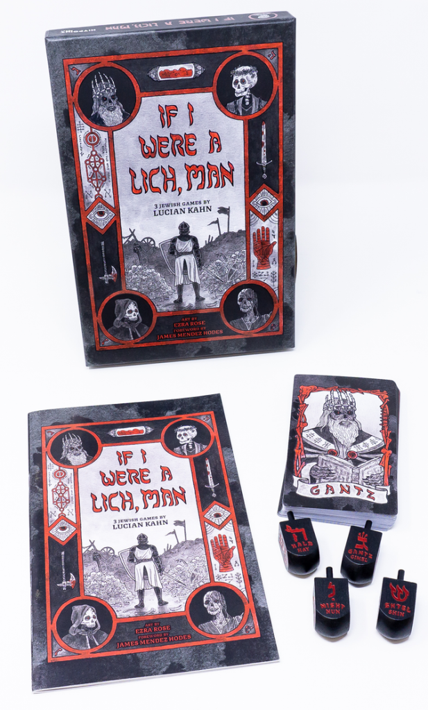 Image ID: The box set of "If I Were a Lich, Man" with its contents out for display. The box is propped up in the background and lying in front of it is the rule booklet, which contains the rules for the three games, a pile of all the cards used in the various games, one of the lich cards is on top, and four dreidels, each one with a different Hebrew letter facing up. End ID. 