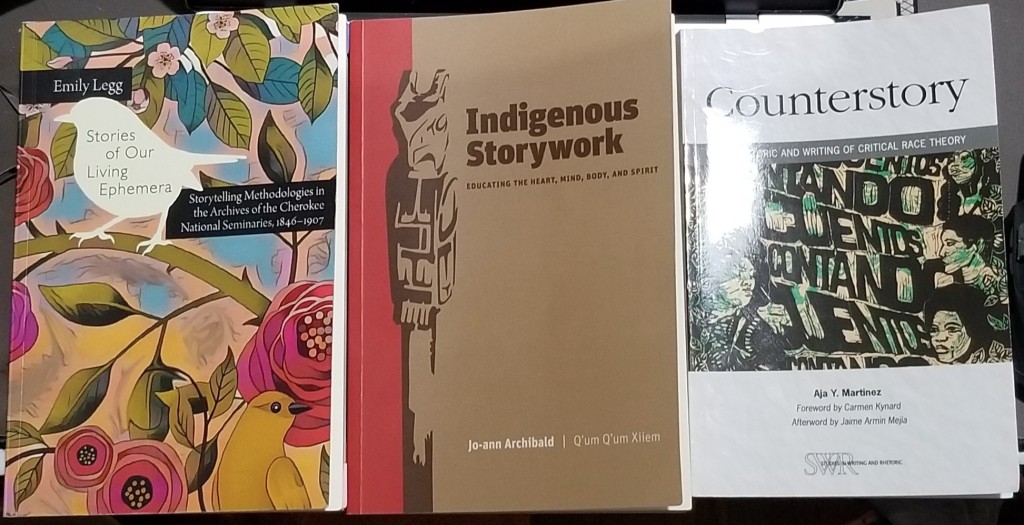 Image ID: Three books laid out next to each other. From left to right they are, "Stories of our Living Ephemera: Storytelling Methodologies in the Archives of the Cherokee National Seminaries, 1846-1907" by Emily Legg, "Indigenous Storywork: Educating the Heart, Mind, Body, and Spirit" by Jo-ann Archibald, and "Counterstory: The Rhetoric and Writing of Critical Race Theory" by Aja Y. Martinez. End ID. 